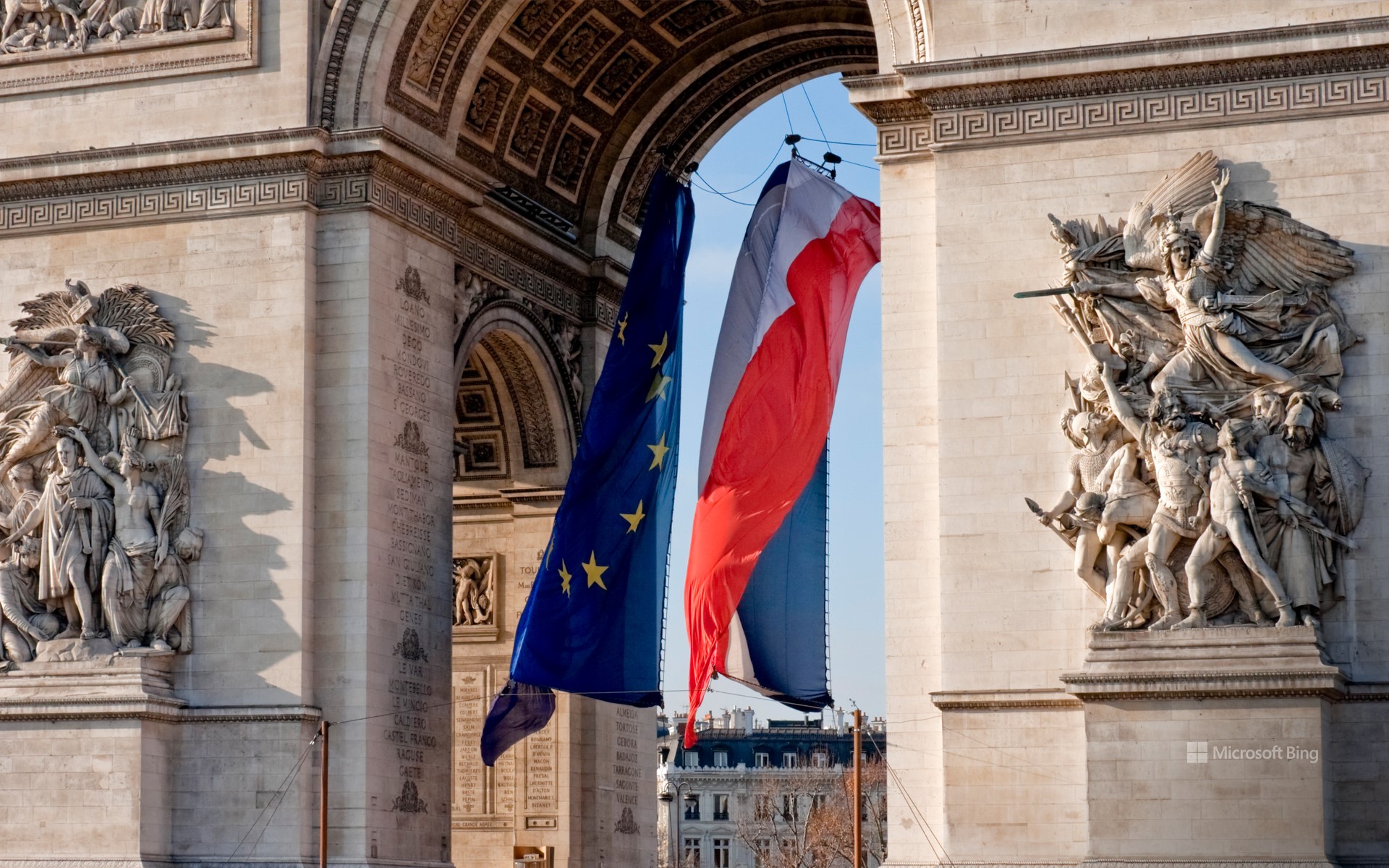 Flags of France and Europe fluttering under the Arc de Triomphe, Paris