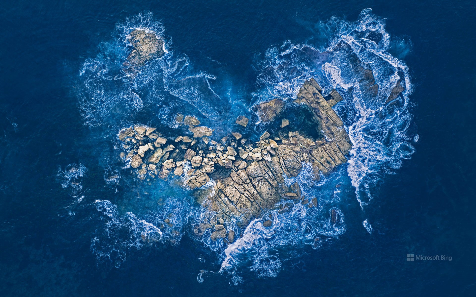 Ocean waves crashing over a heart-shaped rock island off the coast of Sydney, Australia